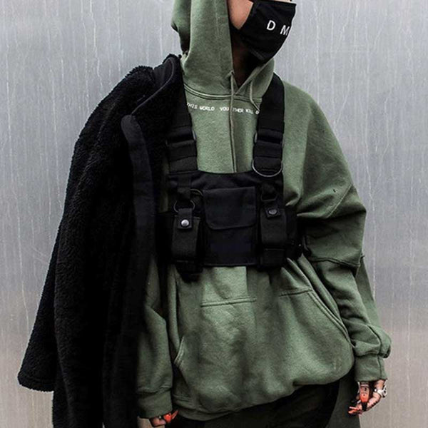 A man wearing a black chest rig bag with a green hoodie